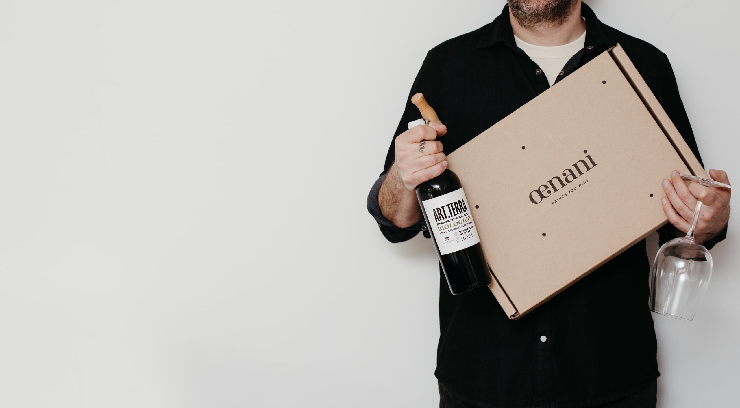 Man met een oenani wijnbox in een witte achtegrond met een fles wijn in een hand en een glas wijn in de andere
